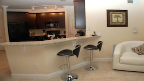 A kitchen with dark wooden cabinets, a central island with bar stools, and a white sofa with a zebra print pillow. - Ec47ha - 3 Bedroom Condo In Terrace Ridge, Sleeps Up To 6, Just 6 Miles To Disney (Davenport)