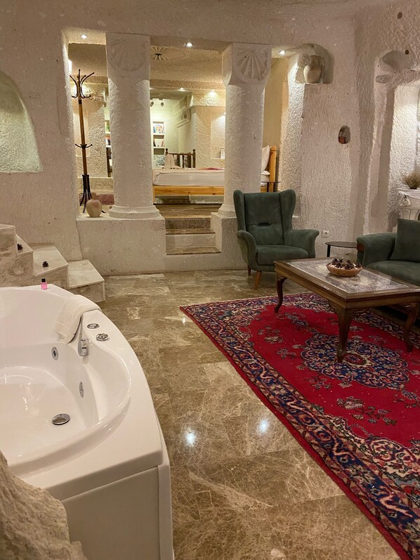 Una habitación amplia con una bañera grande, un sillón verde, una mesita de café y un tapete rojo estampado.