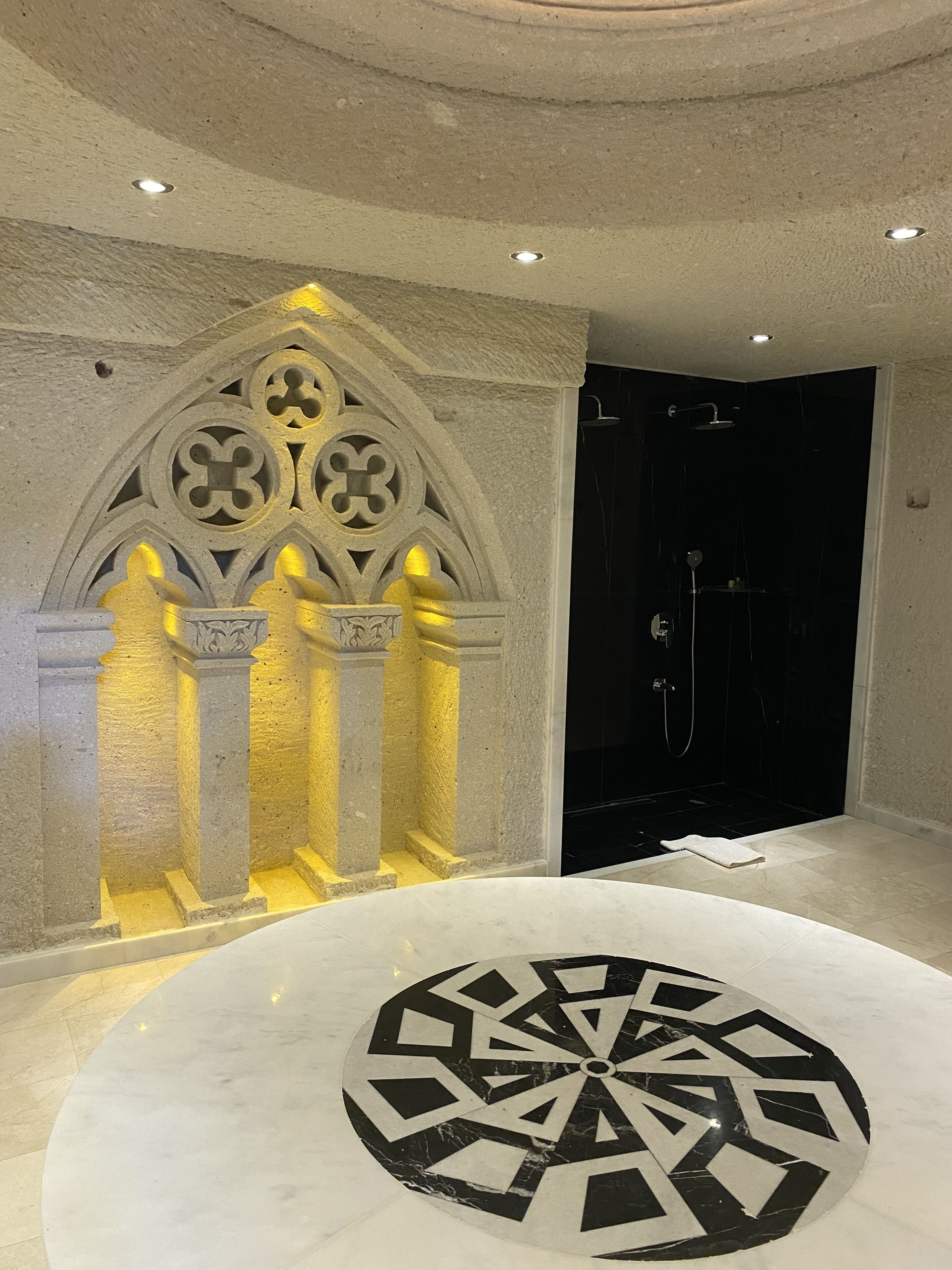 A modern bathroom with a circular patterned floor, a shower area, and a decorative stone archway.