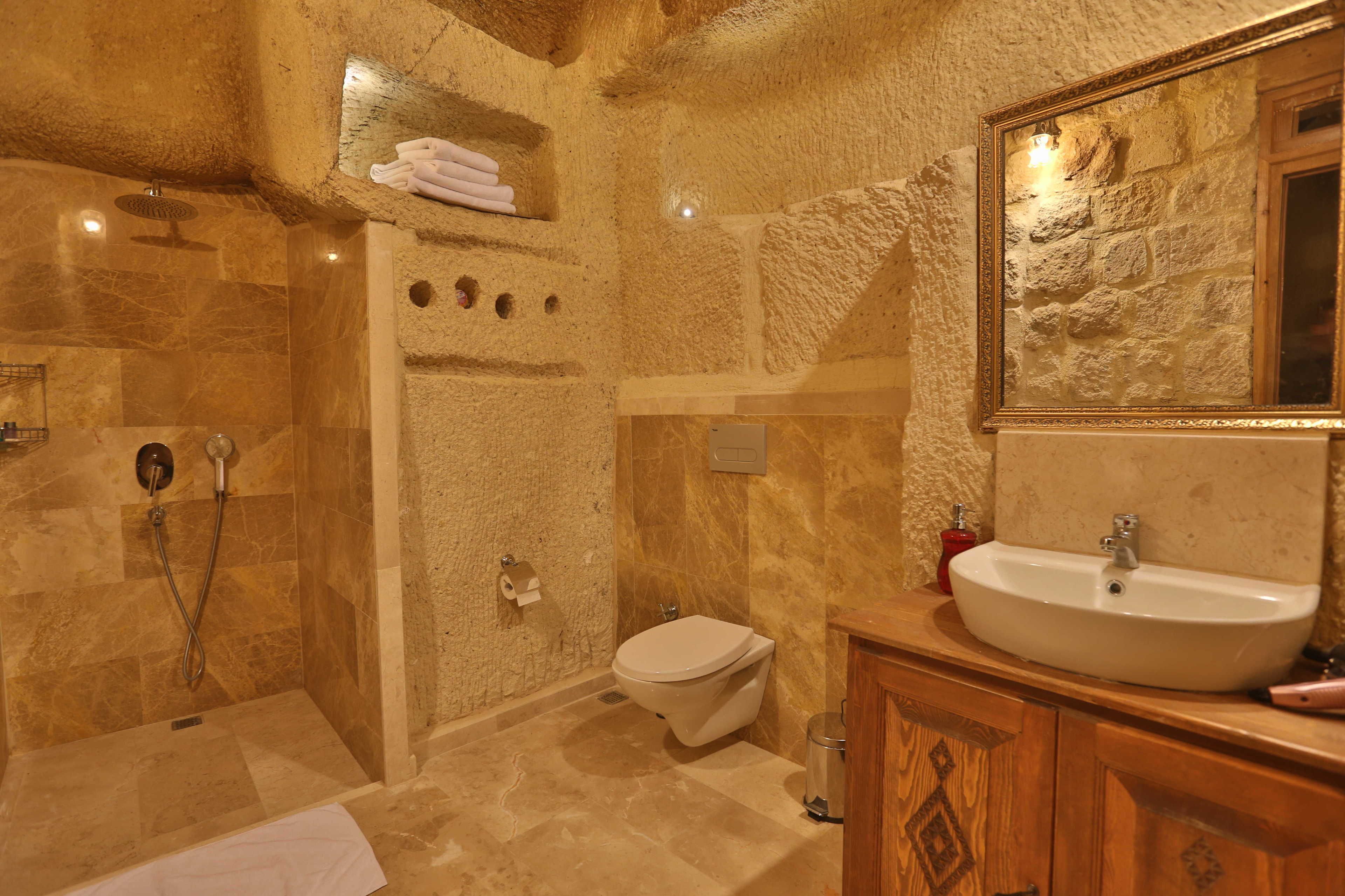 A bathroom with a stone wall, a shower, a toilet, and a sink with a mirror.