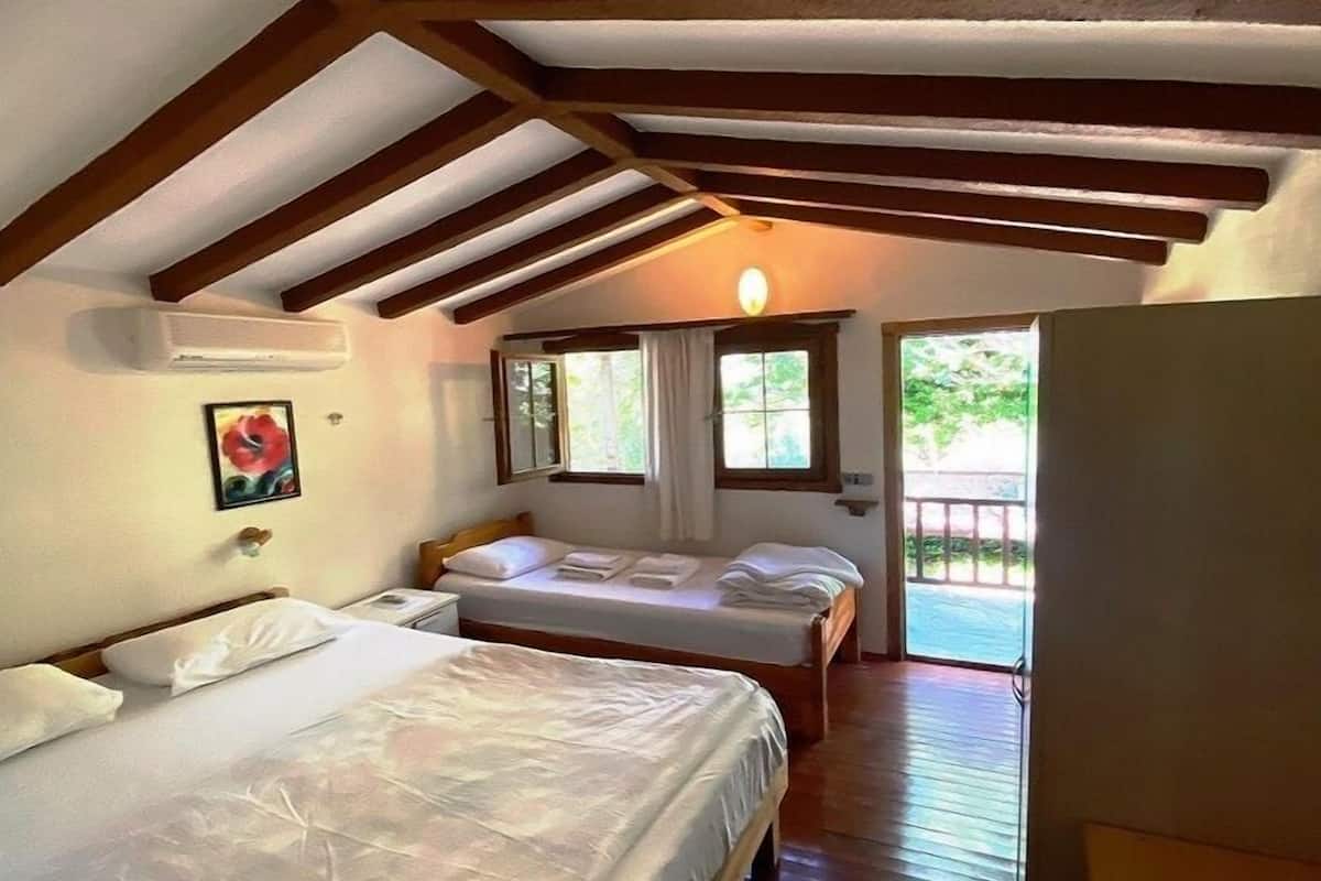 A bedroom with two beds, wooden beams on the ceiling, a window, and a door leading outside.