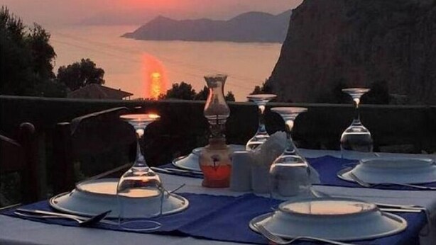 A table set for dinner with a view of the sunset over the sea and a mountain in the background. - Montenegro Motel (Fethiye)