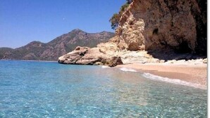 A clear coastal beach with rocky formations and a mountain in the background. - Montenegro Motel (Fethiye)