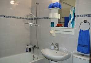 A bathroom with a bathtub, a sink, and a toilet. There are toiletries on the wall and a towel rack.