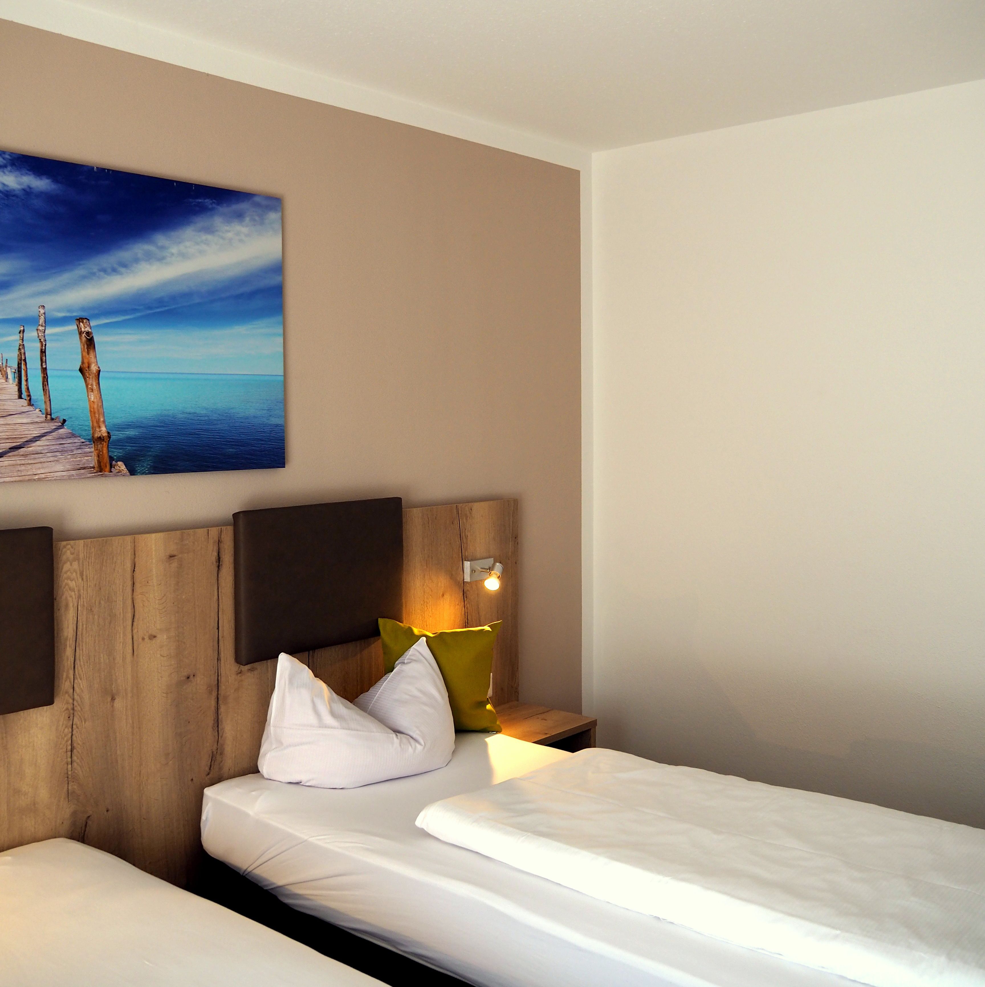 Une chambre d’hôtel avec une tête de lit en bois, un tableau représentant une scène de plage, une lampe de chevet et un lit parfaitement fait.