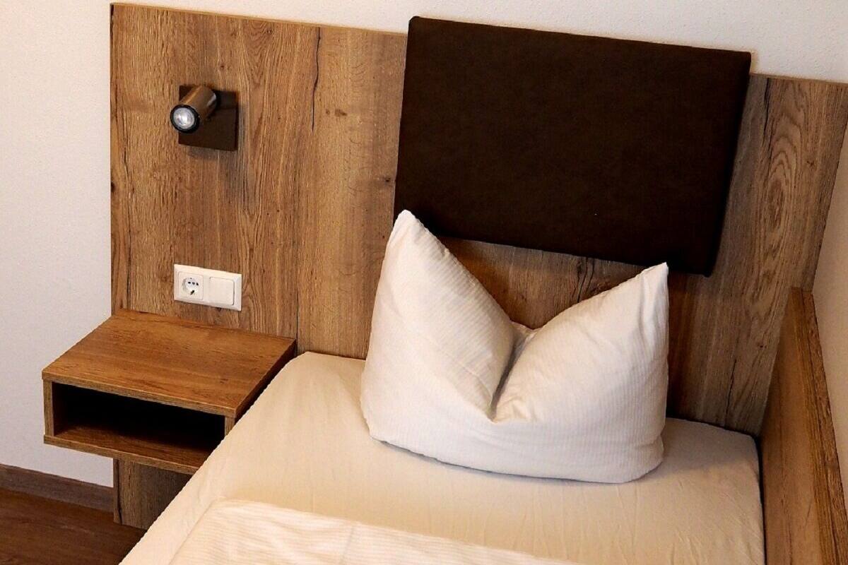 A single bed with a wooden headboard, a bedside table, and a power outlet.