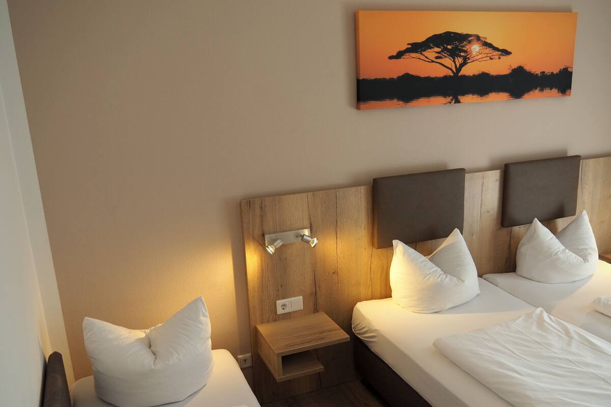 A hotel room with two beds, a nightstand, a wooden headboard, and a wall-mounted light fixture.