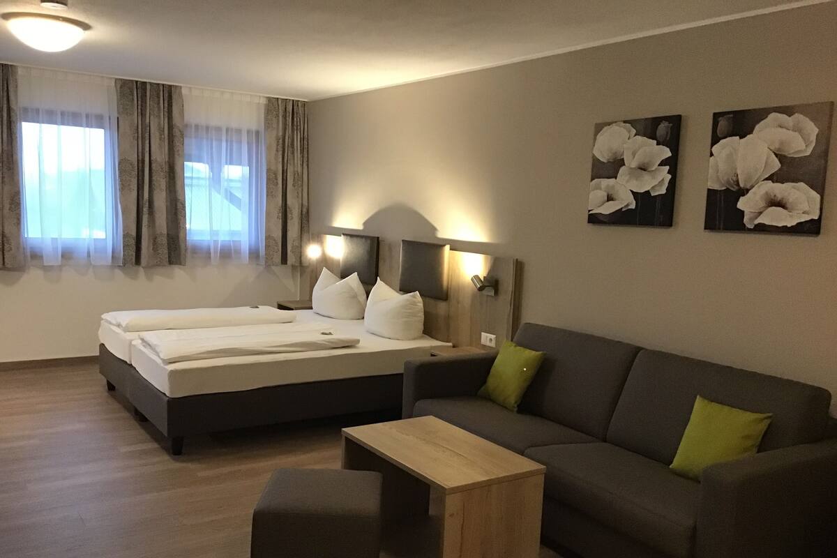 A hotel room with a bed, a sofa, a small table, and artwork on the wall.