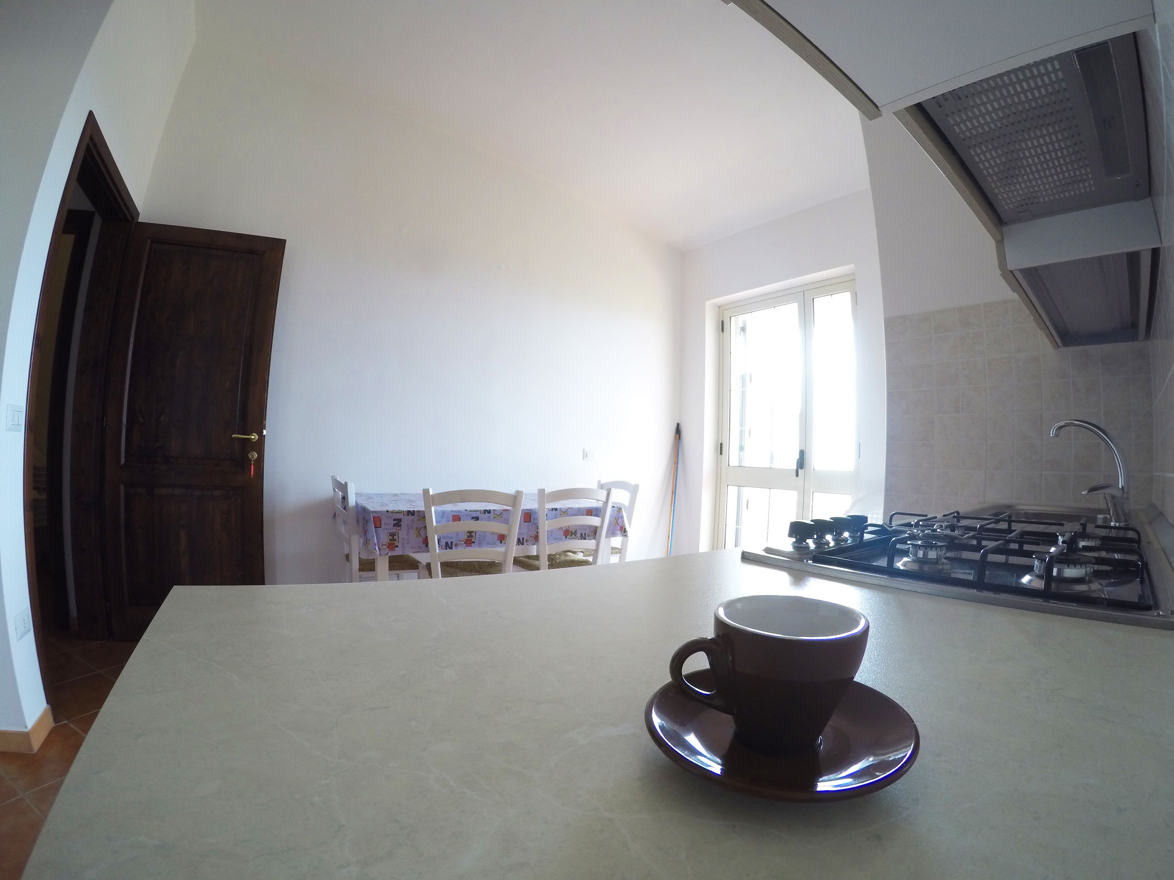 A kitchen with a coffee cup on the counter, a dining table with chairs, and a stove.