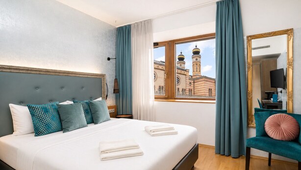 A hotel room with a bed, a chair, a large window with a view of a building, and a mirror. - Hotel Memories Budapest (Budapest)