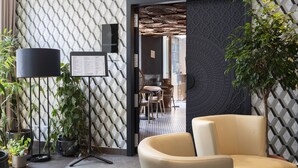 A modern interior with a geometric patterned wall, a black-framed lamp, a menu stand, and a seating area with a beige chair. - Hotel Memories Budapest (Budapest)