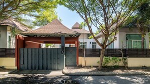 Ein verschlossenes Tor mit einem überdachten Schutzhaus, eine gepflasterte Straße und ein Baum im Vordergrund.