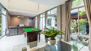 Ein modernes Wohnzimmer mit Billardtisch, einer Couch und einem großen Fenster mit Blick ins Freie.
