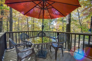 Une terrasse en bois avec une table et des chaises en verre, entourée d’arbres aux feuilles d’automne.