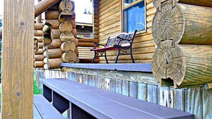 A rustic wooden cabin with a wooden bench and picnic table outside, a window with a view, and a decorative log wall. - Cajun Cedar Log Cottages 1 bdrm. - Unit 5 (Margaree Harbour)