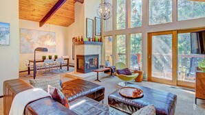 A spacious living room with a fireplace, leather sofas, a dining area with a map on the wall, and large windows offering a view of the outdoors. - Tannenbaum By The River 2 Bedroom Condo by RedAwning (Breckenridge)