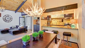A modern living room with a dark wooden dining table, two potted plants, and a chandelier. - Tannenbaum By The River 2 Bedroom Condo by RedAwning (Breckenridge)