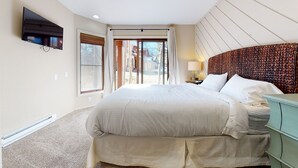 Ein Hotelzimmer mit einem großen Bett, einem an der Wand befestigten Fernseher, einem Fenster mit Vorhängen und Blick nach draußen.
