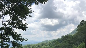 Un sentier de pierres serpente à travers un paysage verdoyant et luxuriant, parsemé d’une végétation dense, avec des montagnes qui se dessinent à l’horizon.