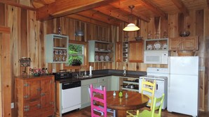 Une cuisine avec des murs en bois, un plafond en bois, un poêle blanc, un réfrigérateur blanc, un meuble en bois et une table ronde avec des chaises.