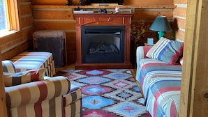 L’intérieur d’une cabane en rondins, avec une cheminée, deux canapés, un téléviseur et un ventilateur de plafond.
