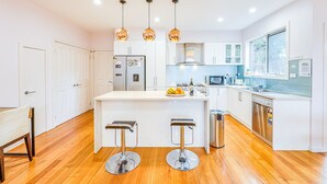 Une cuisine moderne avec des meubles blancs, un îlot central doté de tabourets, un réfrigérateur en acier inoxydable et des luminaires suspendus.