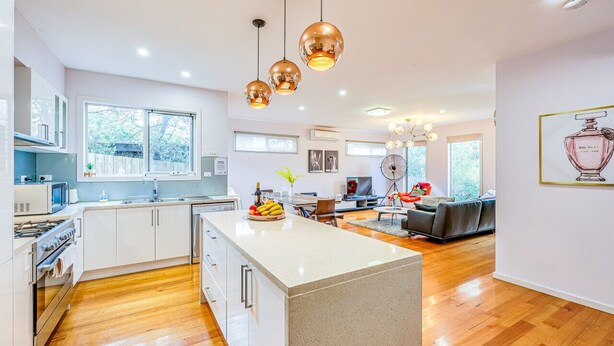 Une cuisine moderne avec des meubles blancs, un îlot central et des luminaires suspendus.
