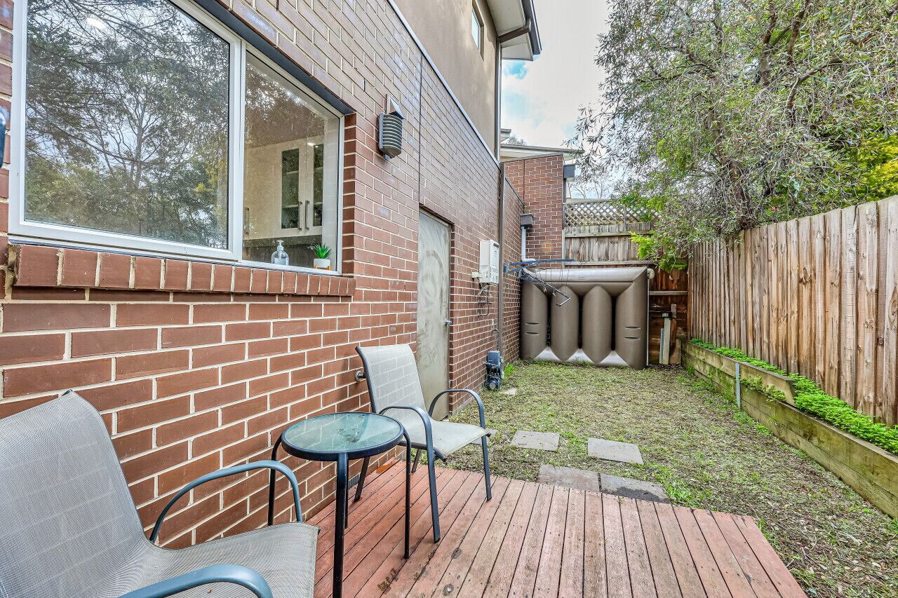A backyard with a brick wall, a wooden deck, a metal table, and a chair.
