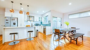 Une cuisine moderne avec des meubles blancs, un îlot central doté de tabourets et des luminaires suspendus.
