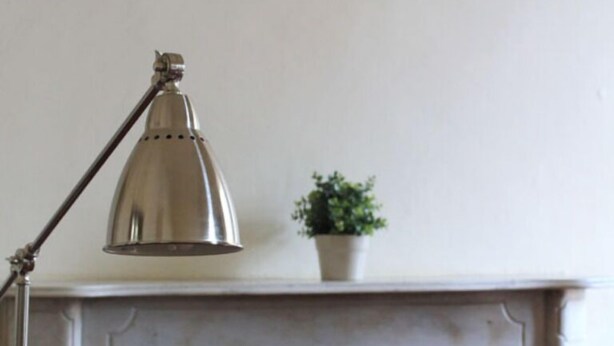A table with a metal desk lamp, a potted plant, and a chair with a carved backrest.