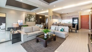 A modern living room with a sofa, coffee table, and a TV. There is a kitchen area in the background. - AnB Pool Villa Modern 3BR at The Ville Jomtian Pattaya (Pattaya)