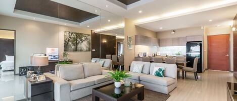 A modern living room with a sofa, coffee table, and a TV. There is a kitchen area in the background.