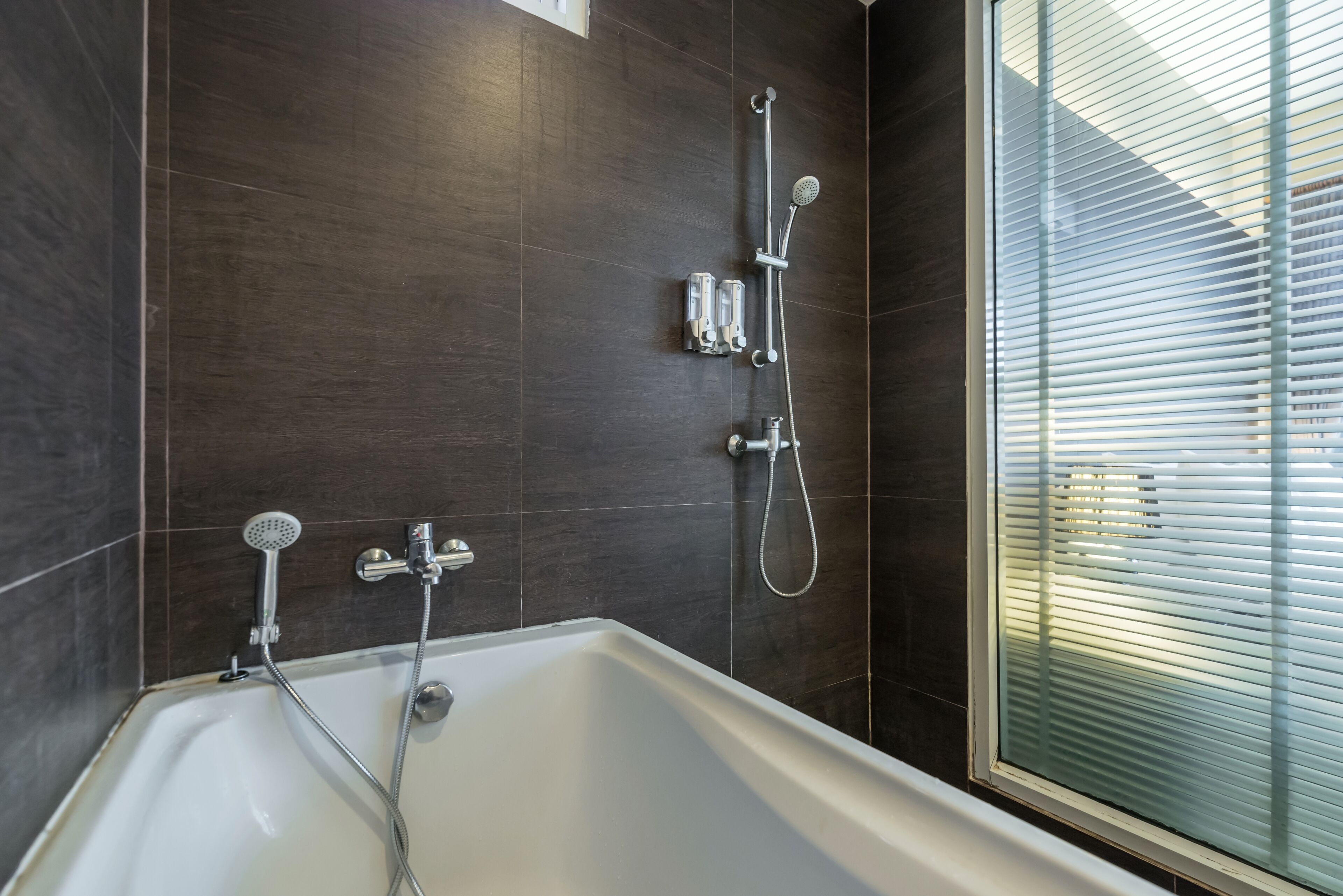 Un baño moderno con bañera, ducha y ventana con persianas.