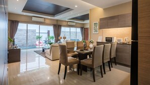 A modern living room with a dining area, large windows with curtains, a kitchen with a microwave, and a view of the sea. - AnB Pool Villa Modern 3BR at The Ville Jomtian Pattaya (Pattaya)