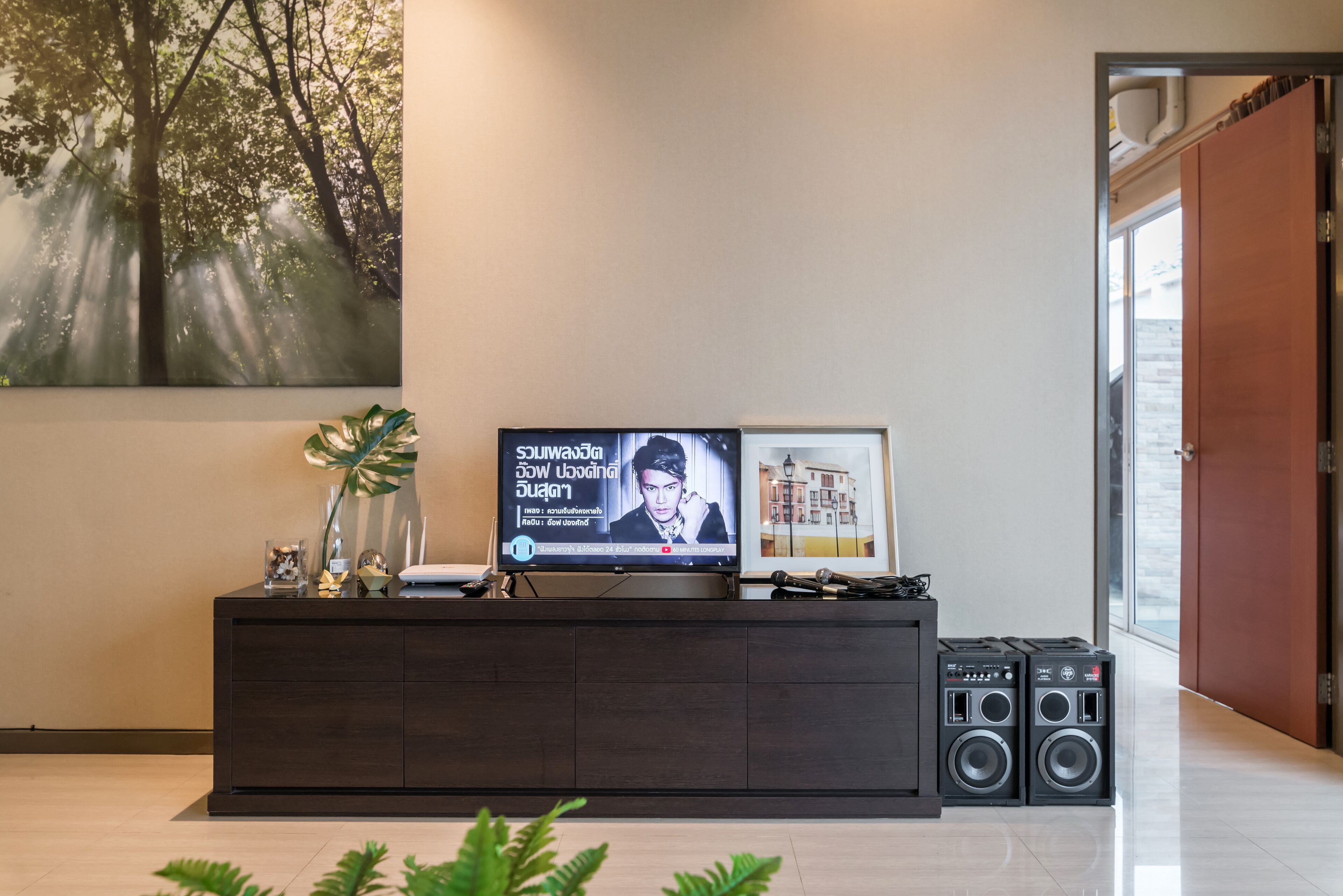 Un salon moderne avec un téléviseur à écran plat posé sur une console en bois foncé, un tableau encadré et deux haut-parleurs noirs.