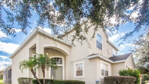 A single-story house with a beige exterior, a front entrance with an arched doorway, and a small front yard with a palm tree and shrubs. - Ip60299 - Highlands Reserve - 5 Bed 2.5 Baths Villa (Davenport)