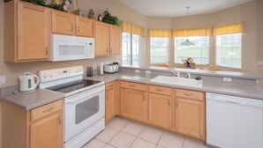 A kitchen with wooden cabinets, a microwave, an oven, a dishwasher, and a window with yellow curtains. - Ip60299 - Highlands Reserve - 5 Bed 2.5 Baths Villa (Davenport)