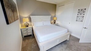 A bedroom with a large bed, two bedside tables with lamps, a door, and a wall with two decorative plates. - Aco254366 - The Encore Club Resort - 5 Bed 5.5 Baths Villa (Kissimmee)