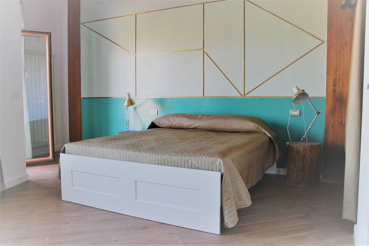 Un dormitorio con cama, dos lámparas de noche, un espejo y un diseño geométrico en la pared.