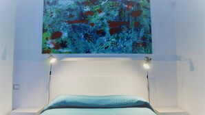 A bedroom with a bed, a white nightstand, and a wall-mounted abstract painting. - Bora B&B (Troia)