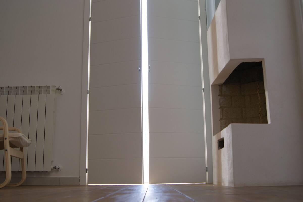 Una habitación con una puerta blanca grande, un radiador, una silla de madera y una chimenea.