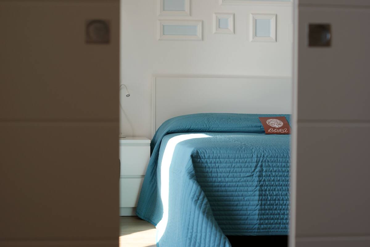 Un dormitorio con una cama cubierta por un edredón azul, un cabecero blanco y una pequeña señal sobre la cama.