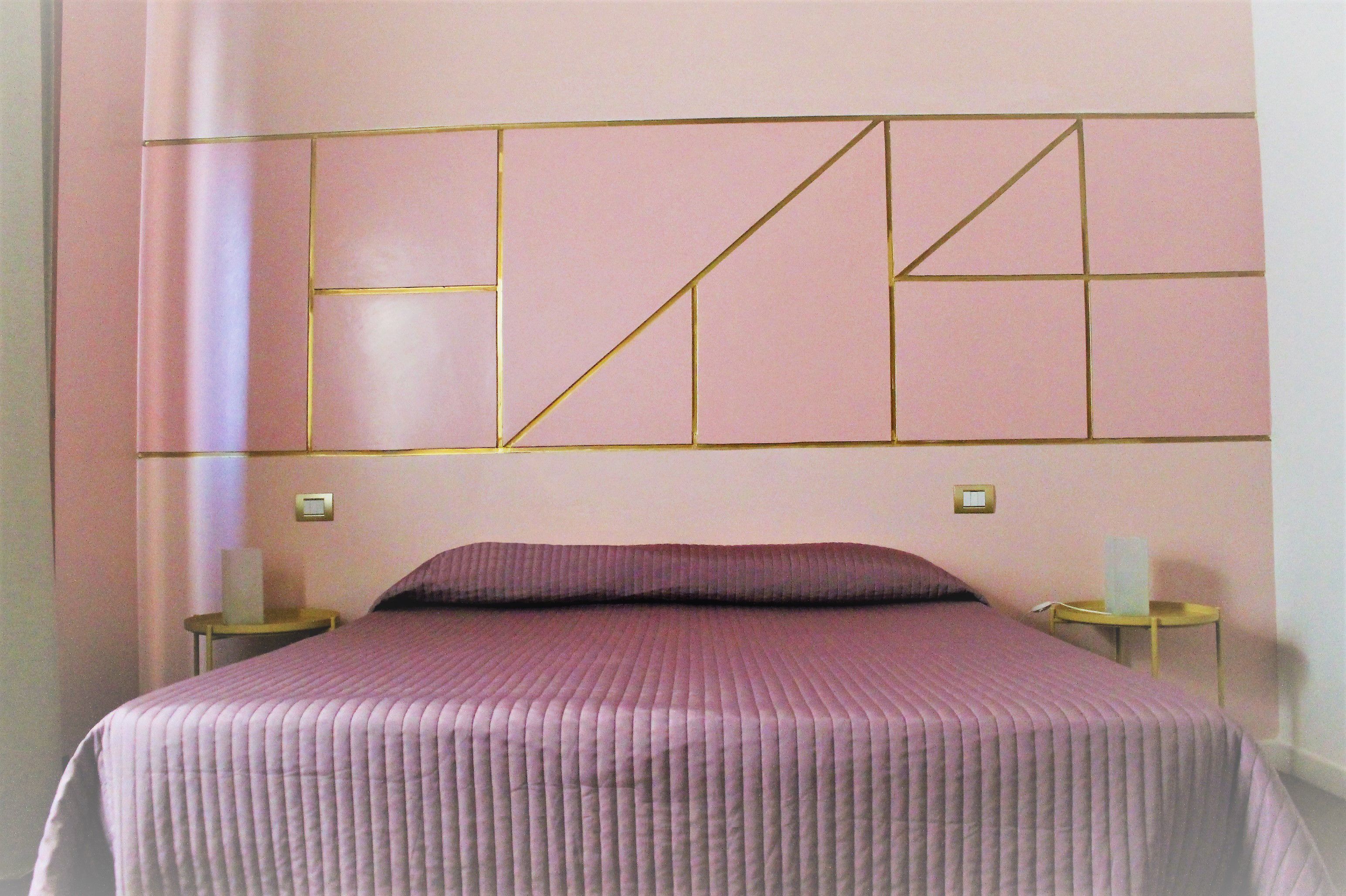 A neatly made bed with a pink bedspread and a headboard with geometric patterns.
