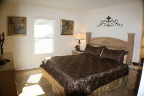 A bedroom with a large bed, two bedside tables, a nightstand, a lamp, and two framed pictures on the wall.
