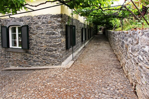 Une ruelle étroite pavée de pierres, avec des murs en pierre et des volets noirs aux fenêtres.