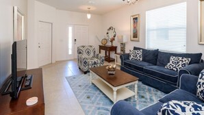 A living room with a dark blue sofa, a patterned armchair, a coffee table, and a television on a wooden stand.