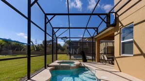 A swimming pool with a hot tub, surrounded by a covered patio area with chairs and a table.