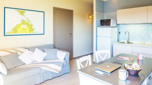 A modern living room with a sofa, a dining table with a laptop, a basket of snacks, and a coffee mug. - Golfo Aranci - apartment for 2 people, directly on the beach, with terrace and sea-view (Golfo Aranci)