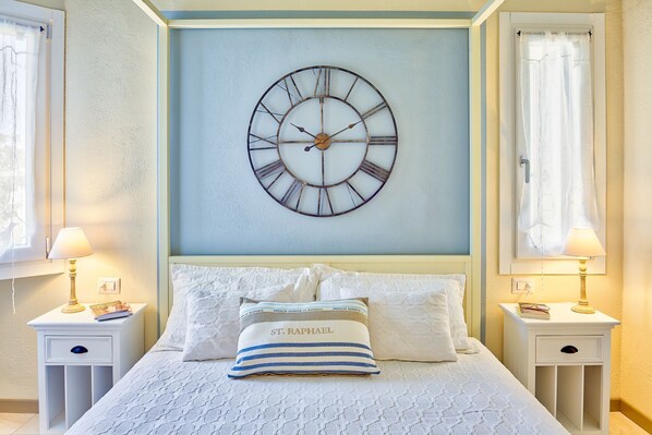 Une chambre à coucher avec une grande horloge murale, un lit avec une literie blanche et deux tables de chevet avec des lampes.