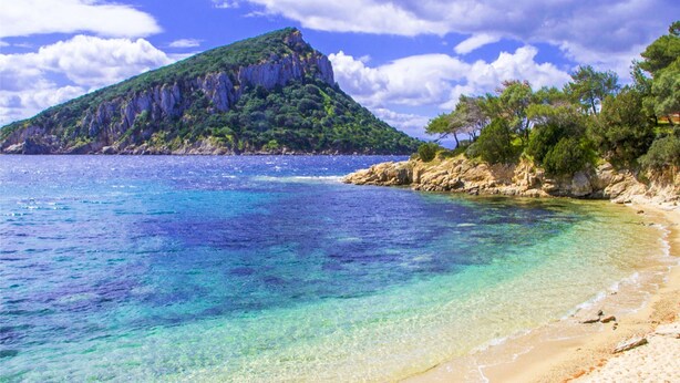 A beach with clear turquoise water, a sandy shore, and a rocky hill with vegetation. - Golfo Aranci - apartment for 2 people, directly on the beach, with terrace and sea-view (Golfo Aranci)